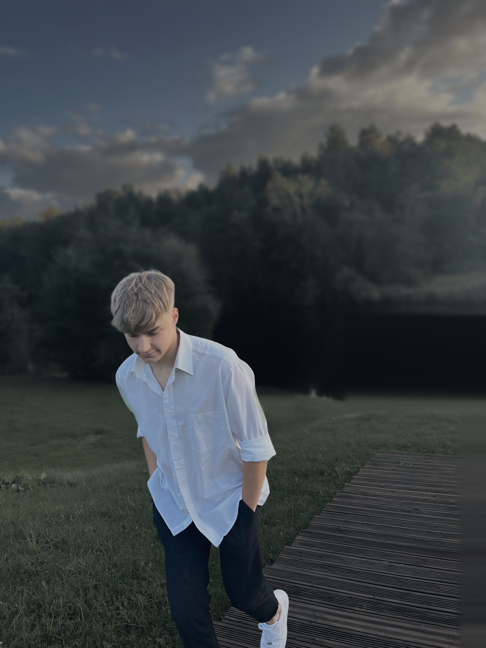 Andre Aadamsoo in a white shirt, walking up a wooden boardwalk by a lake at dusk
