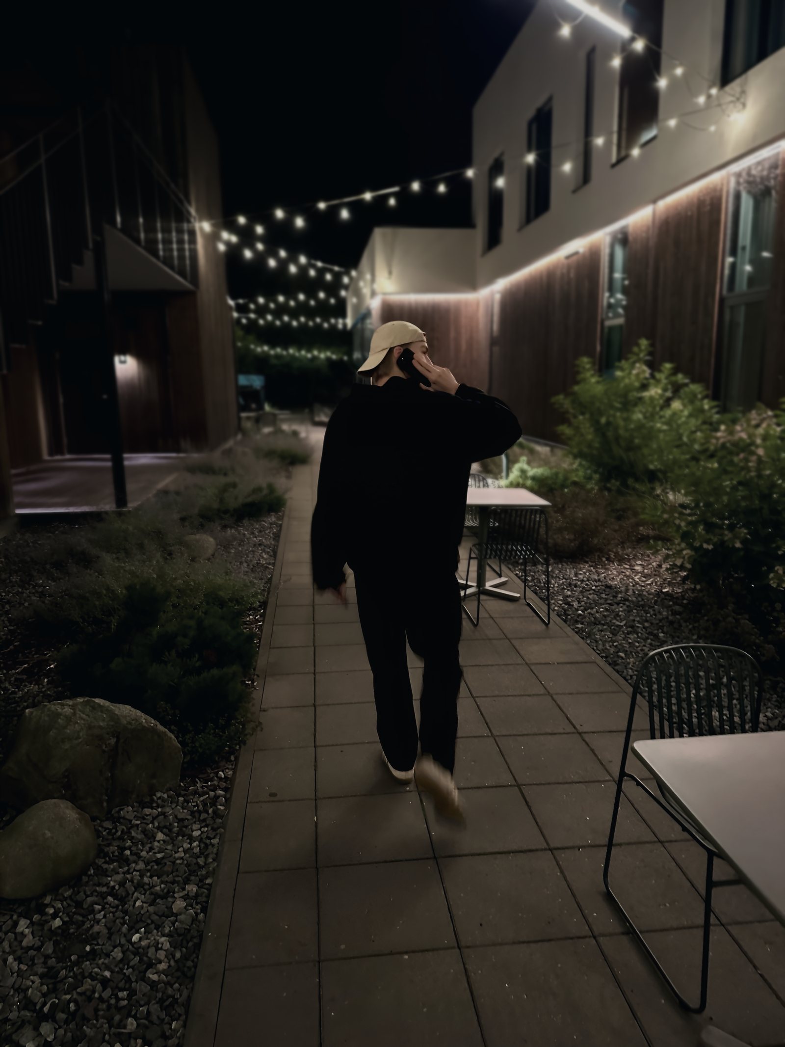 Andre Aadamsoo walking through a courtyard at night under string lights, phone to his ear